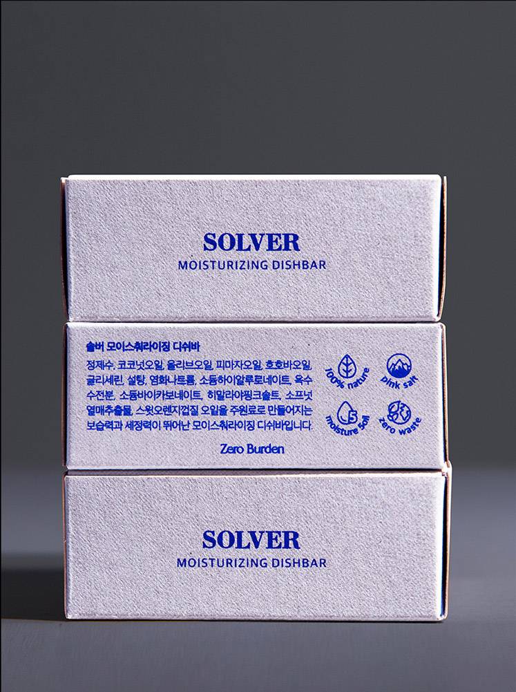 Solver 디쉬바 패키지 세 개를 측면에서 보여주는 장면으로, 각 박스에는 제품명과 함께 주요 성분이 인쇄되어 있음. 패키지 표면의 질감이 자연스러움을 강조하며, 간결한 디자인이 제품의 친환경적 이미지를 잘 나타내고 있음. 하단의 작은 아이콘들은 제품의 특징을 시각적으로 표현함