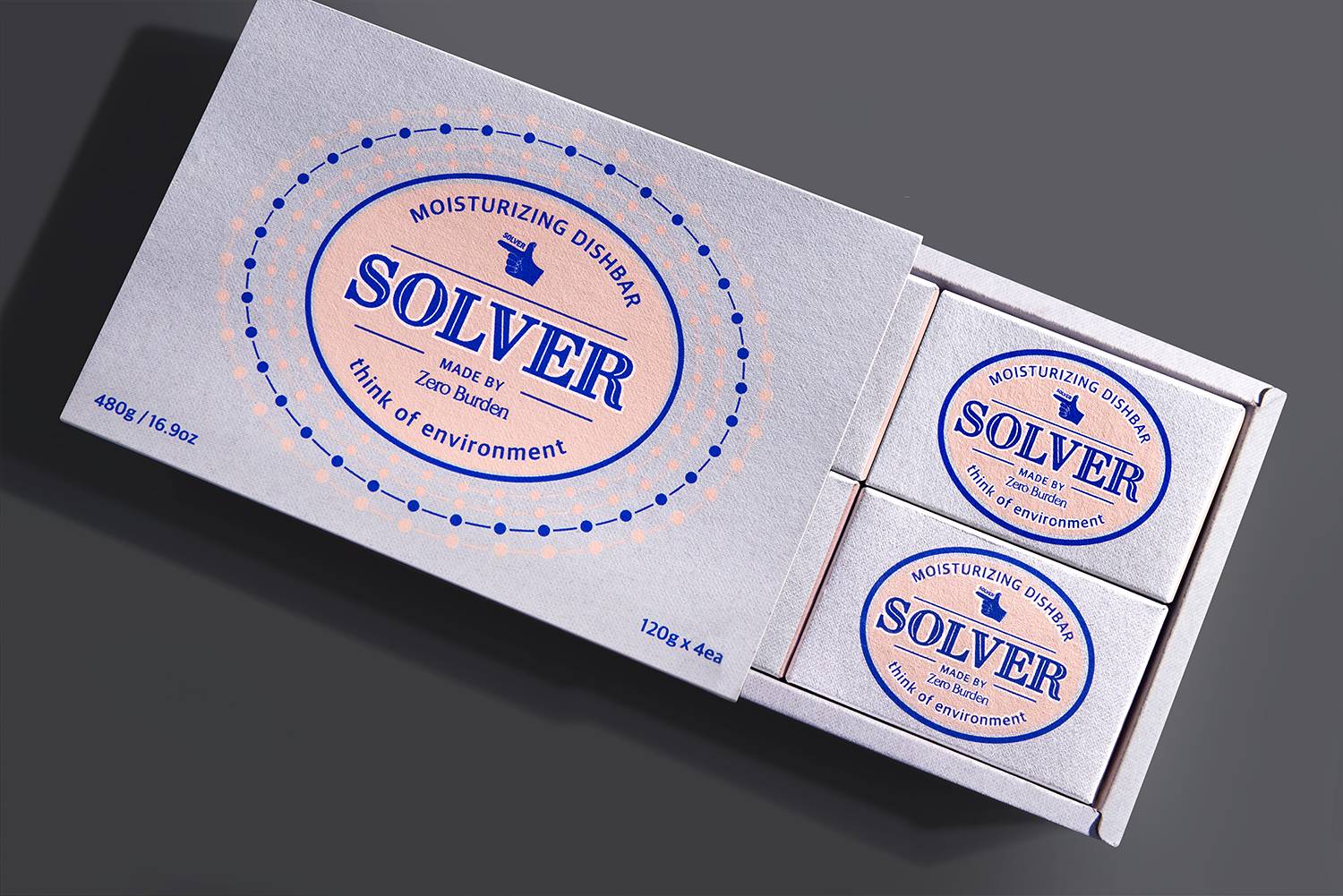 Solver 디쉬바 패키지의 클로즈업으로, 박스가 열려 안에 4개의 작은 비누 패키지가 정렬되어 있는 모습이 보임. 각 비누 패키지에는 동일한 로고 디자인이 적용되어 있으며, 'think of environment'라는 문구가 하단에 쓰여 있음. 중앙에 위치한 파란색 텍스트가 핑크색 배경과 대비되어 시각적으로 강조됨
